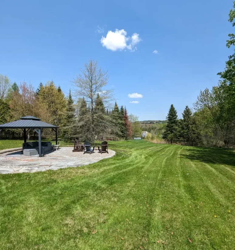 Grand terrain avec motif de tonte rayé, gazebo et chaises Adirondack, entretien de grande surface en Estrie